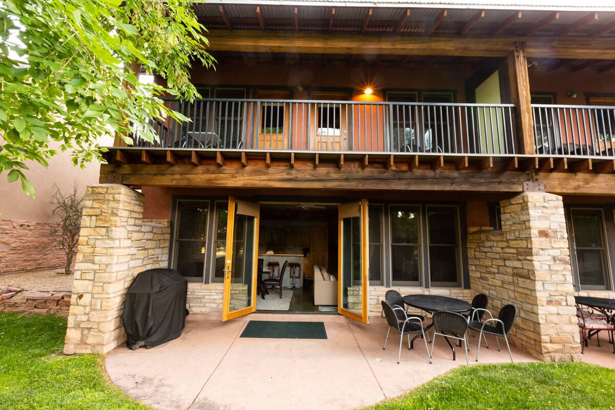 A two-story building with a balcony, stone pillars, and a covered patio area with outdoor furniture.
