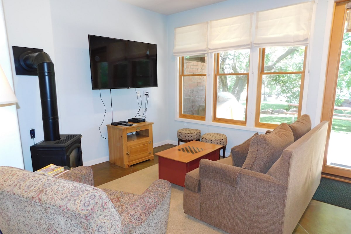A living room with a sofa, a coffee table, a TV, a fireplace, and a window with blinds.