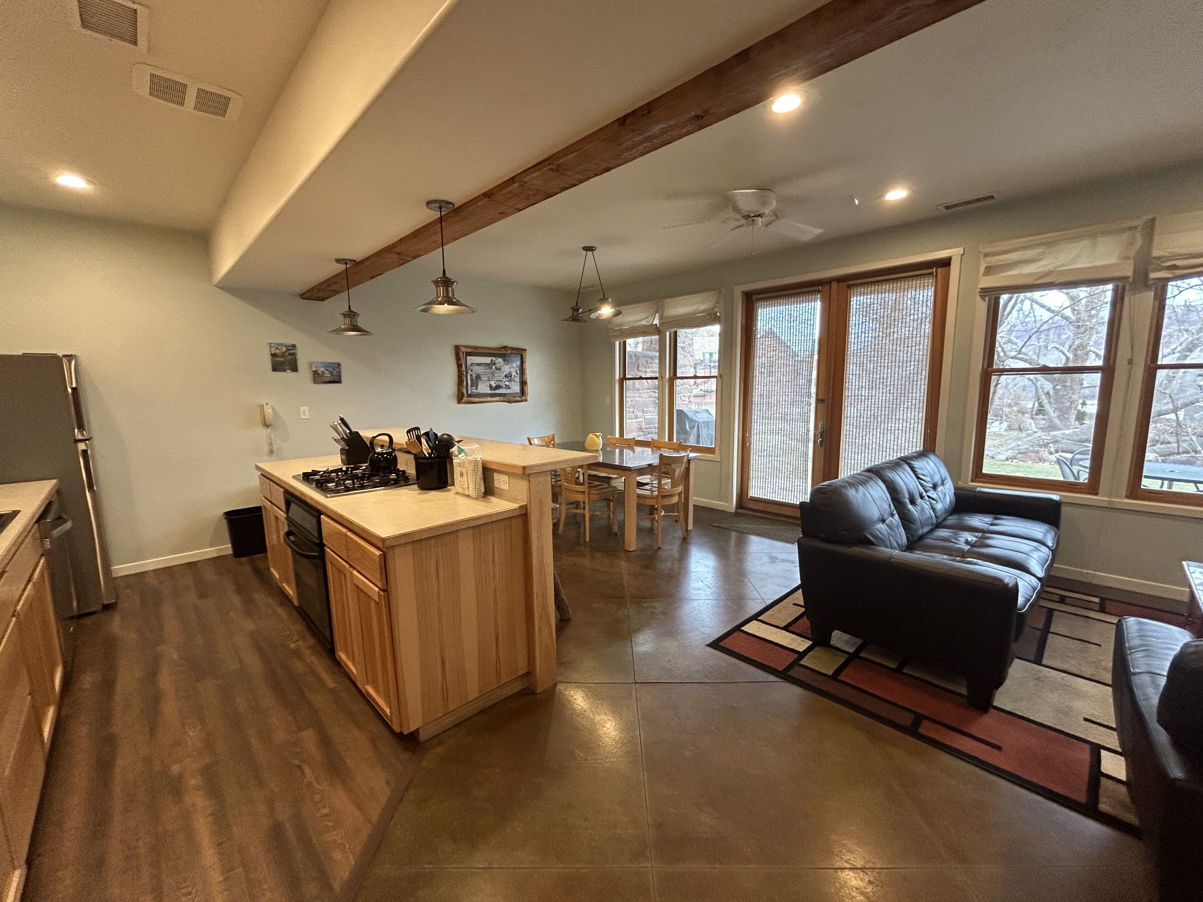 A spacious kitchen with a central island, wooden cabinets, and a dining area with a black leather couch.