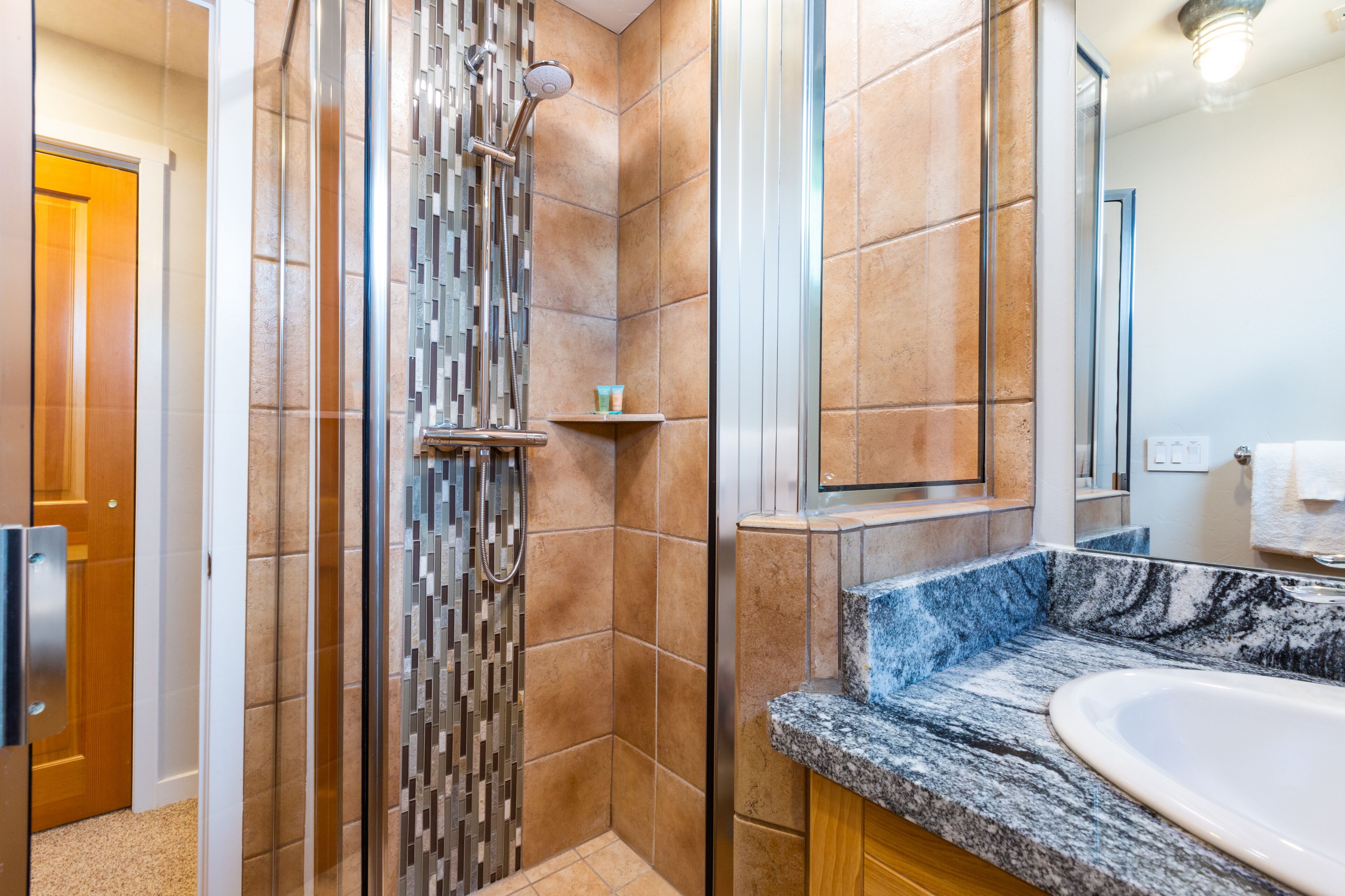 Een moderne badkamer met een douche in een glazen cabine, een marmeren wastafel en een houten kastje.