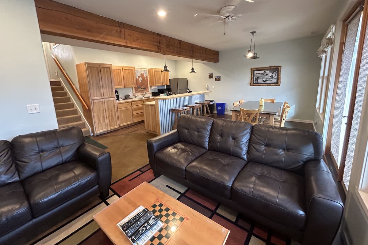 A living room with a sofa, a coffee table with a chessboard, and a kitchen in the background.