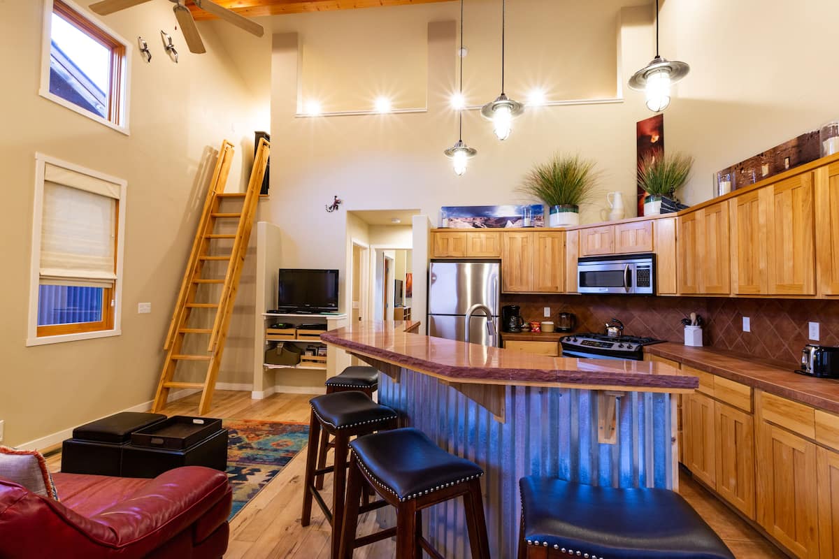 A modern kitchen with wooden cabinets, a central island, bar stools, and a built-in stove.