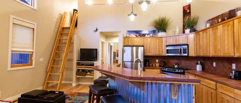 A modern kitchen with wooden cabinets, a central island, bar stools, and a built-in stove.