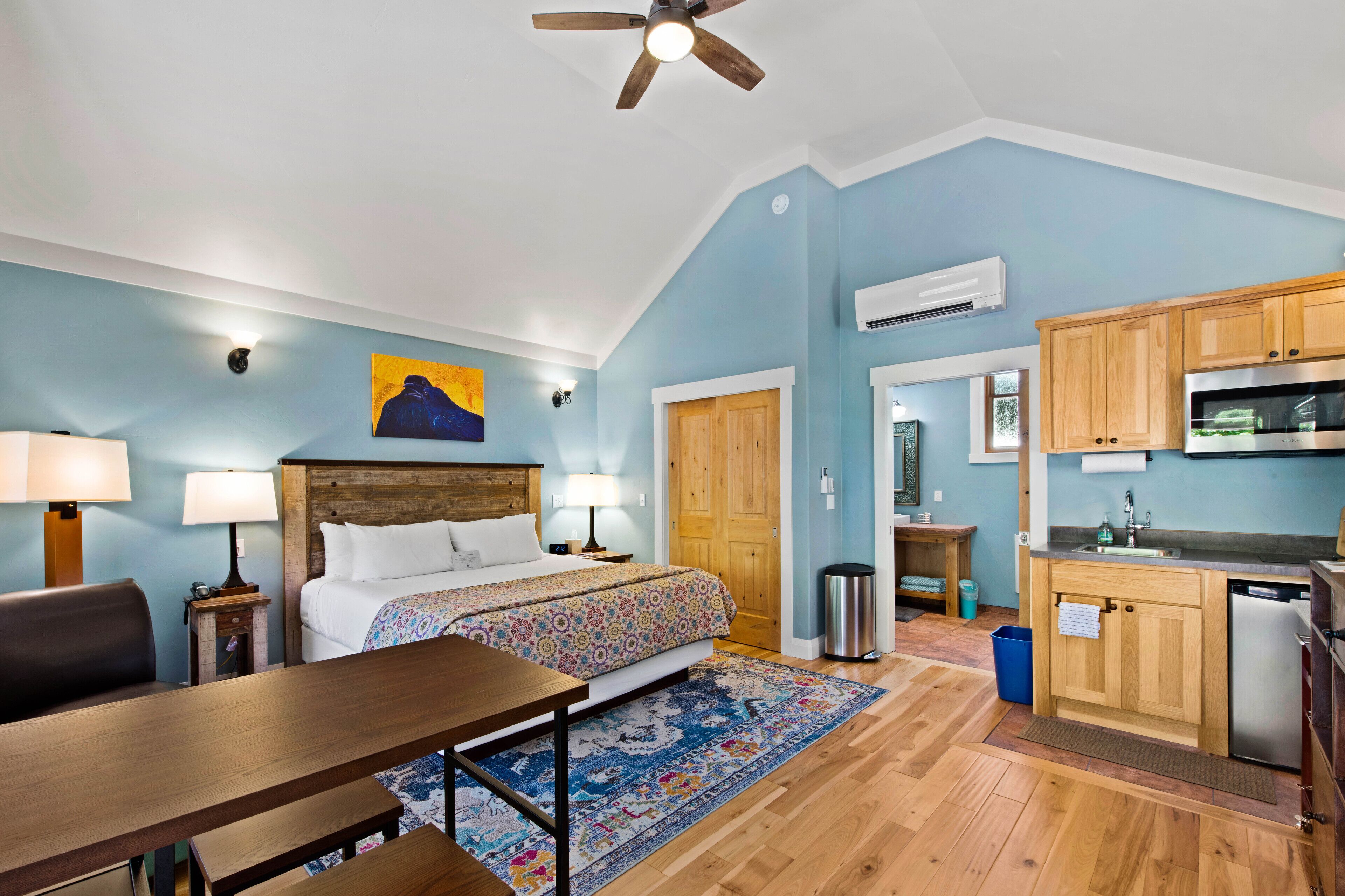 A hotel room with a bed, bedside table, lamp, and a view of the kitchen area.