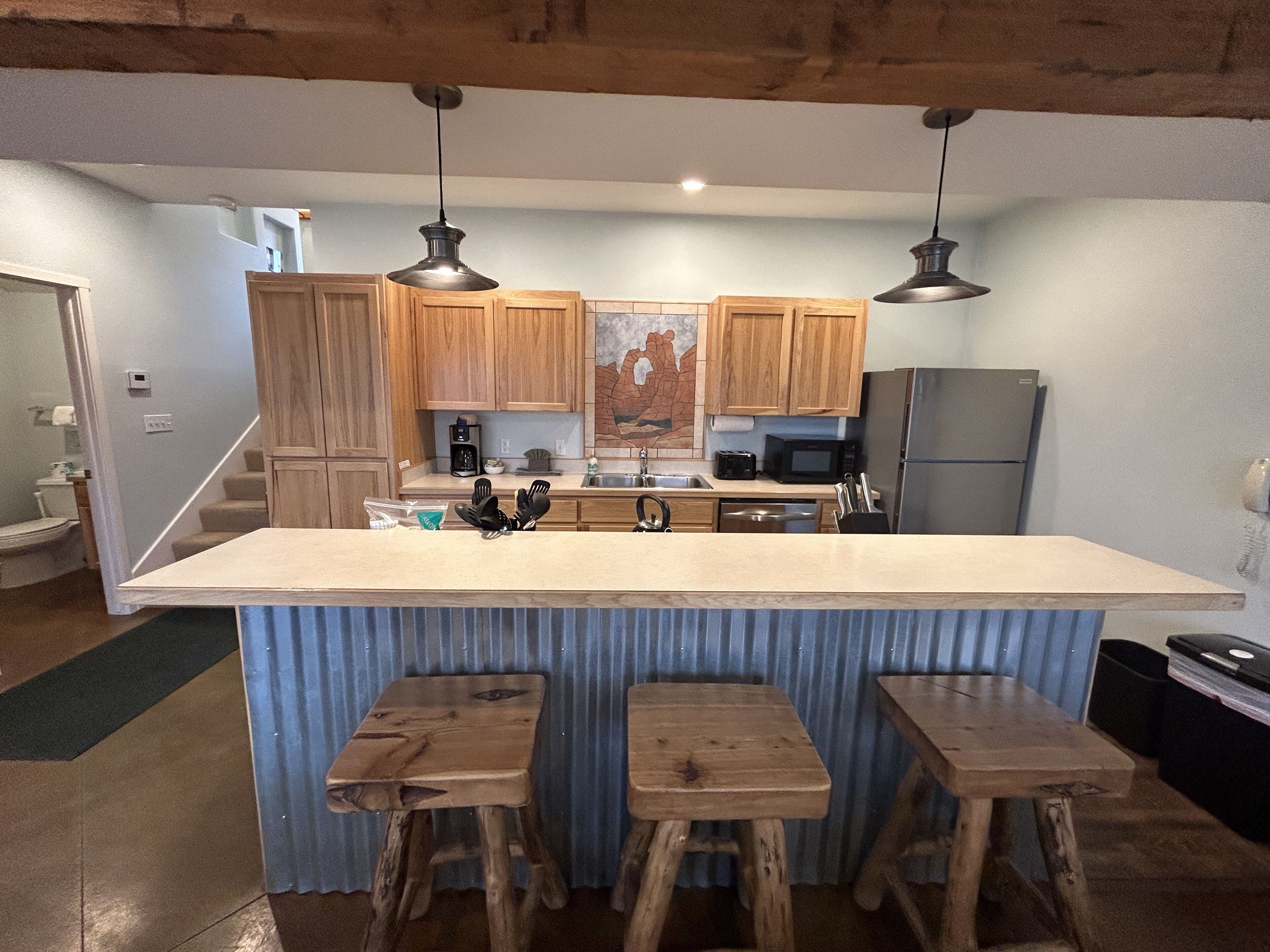 A kitchen with wooden cabinets, a central island with stools, a refrigerator, and a microwave.