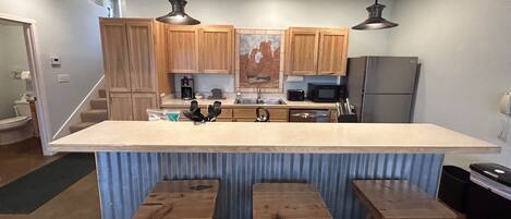 A kitchen with wooden cabinets, a central island with stools, a refrigerator, and a microwave.