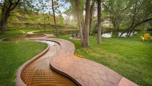 A landscaped garden with a winding water feature, green grass, and yellow chairs. - Moab Springs Ranch (Moab)