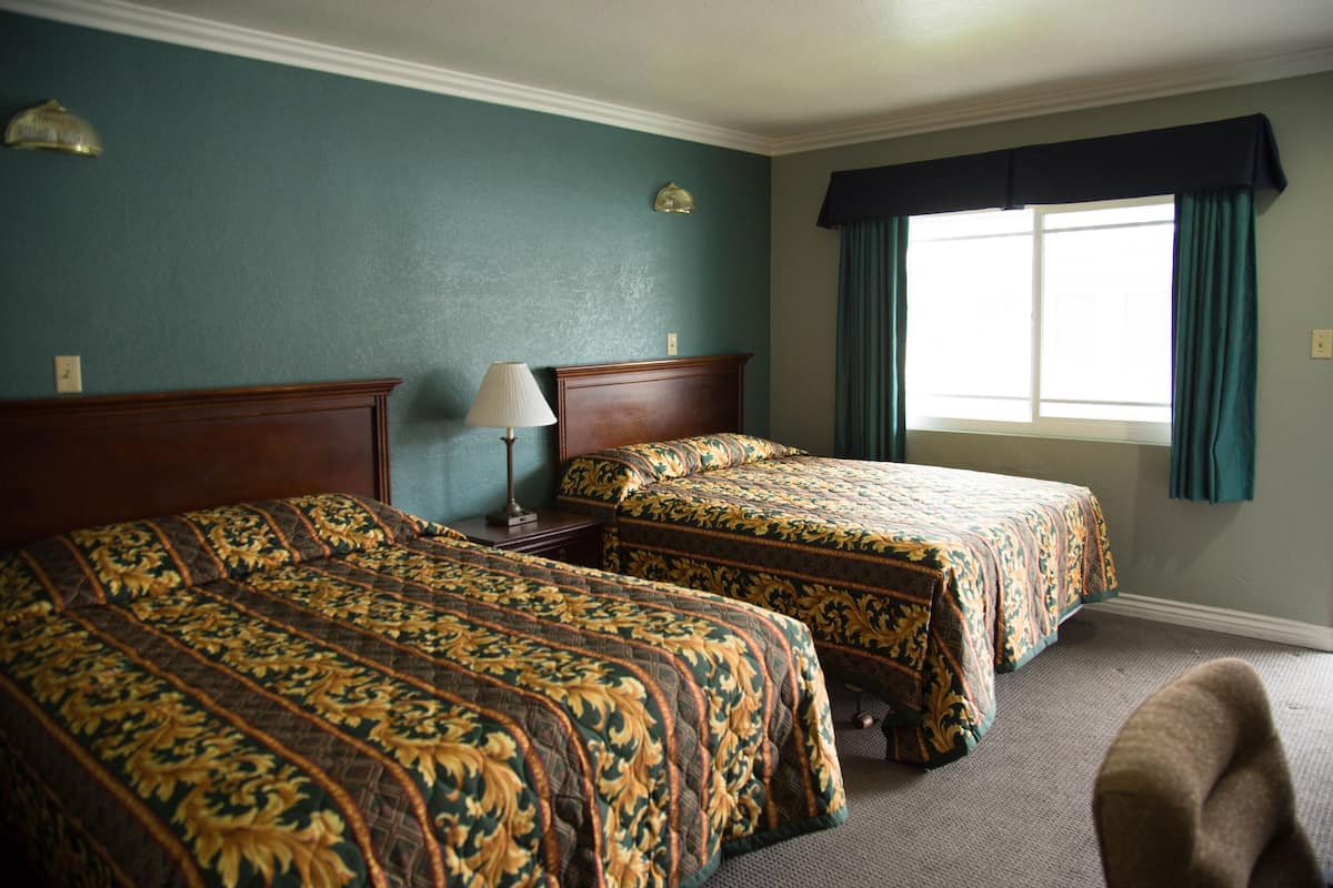 A hotel room with two beds, a nightstand, a lamp, a window with curtains, and a chair.