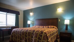 A hotel room with a large bed, two bedside tables with lamps, a desk, and a chair. - Sahara Motel (Anaheim)