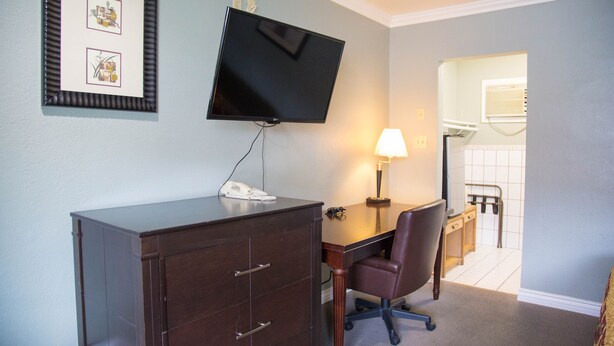 A hotel room with a desk, chair, TV, and a small cabinet. - Sahara Motel (Anaheim)