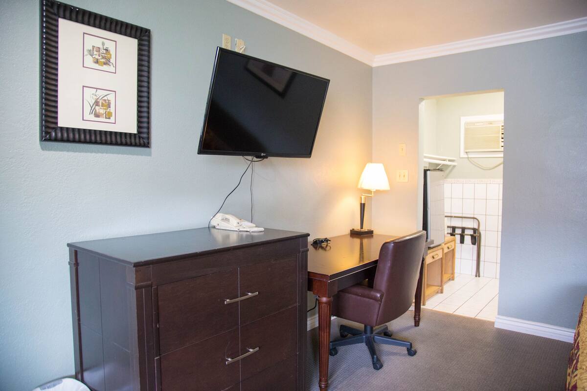 A hotel room with a desk, chair, TV, and a small cabinet.