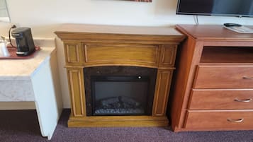 A wooden fireplace with a mantel, a television mounted on the wall above it, and a wooden cabinet to the right.