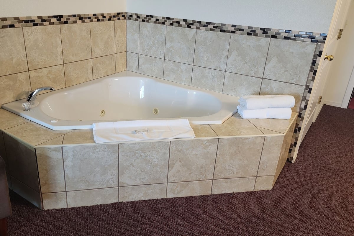 A corner bathtub with a tiled surround, a towel, and a glass.