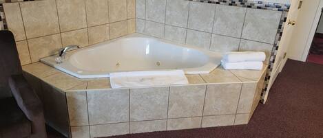 A corner bathtub with a tiled surround, a towel, and a glass.