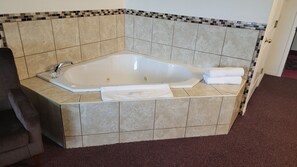 A corner bathtub with a tiled surround, a towel, and a glass.