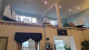 Una habitación con techos altos, molduras decorativas y varios modelos de veleros exhibidos en estanterías.