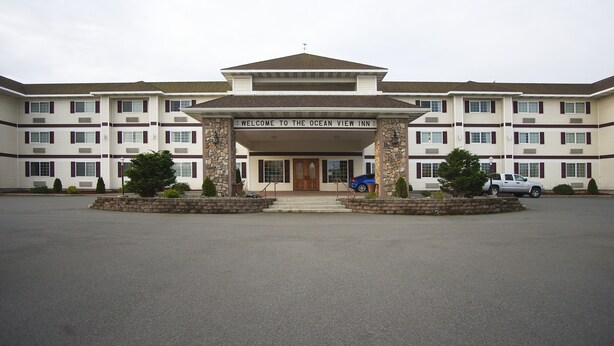 Un hotel de varios pisos con una entrada acogedora, un cartel que dice "Welcome to the Ocean View Inn" y un estacionamiento con algunos coches.