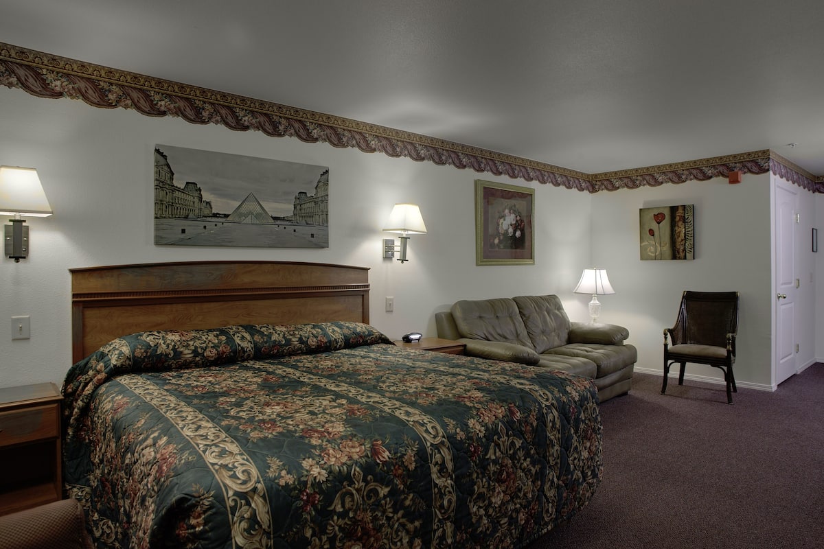 A hotel room with a large bed, a sofa, a chair, and artwork on the walls.