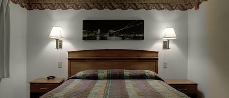 A neatly made bed with a patterned quilt, two bedside tables with lamps, and a cityscape painting on the wall.