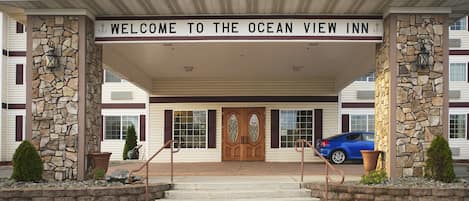 The entrance to the Ocean View Inn with a stone facade, a welcoming sign, and a blue car parked in front.