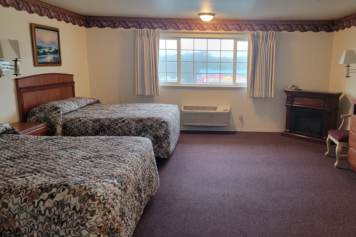 A hotel room with two beds, a television, a desk, and a fireplace.