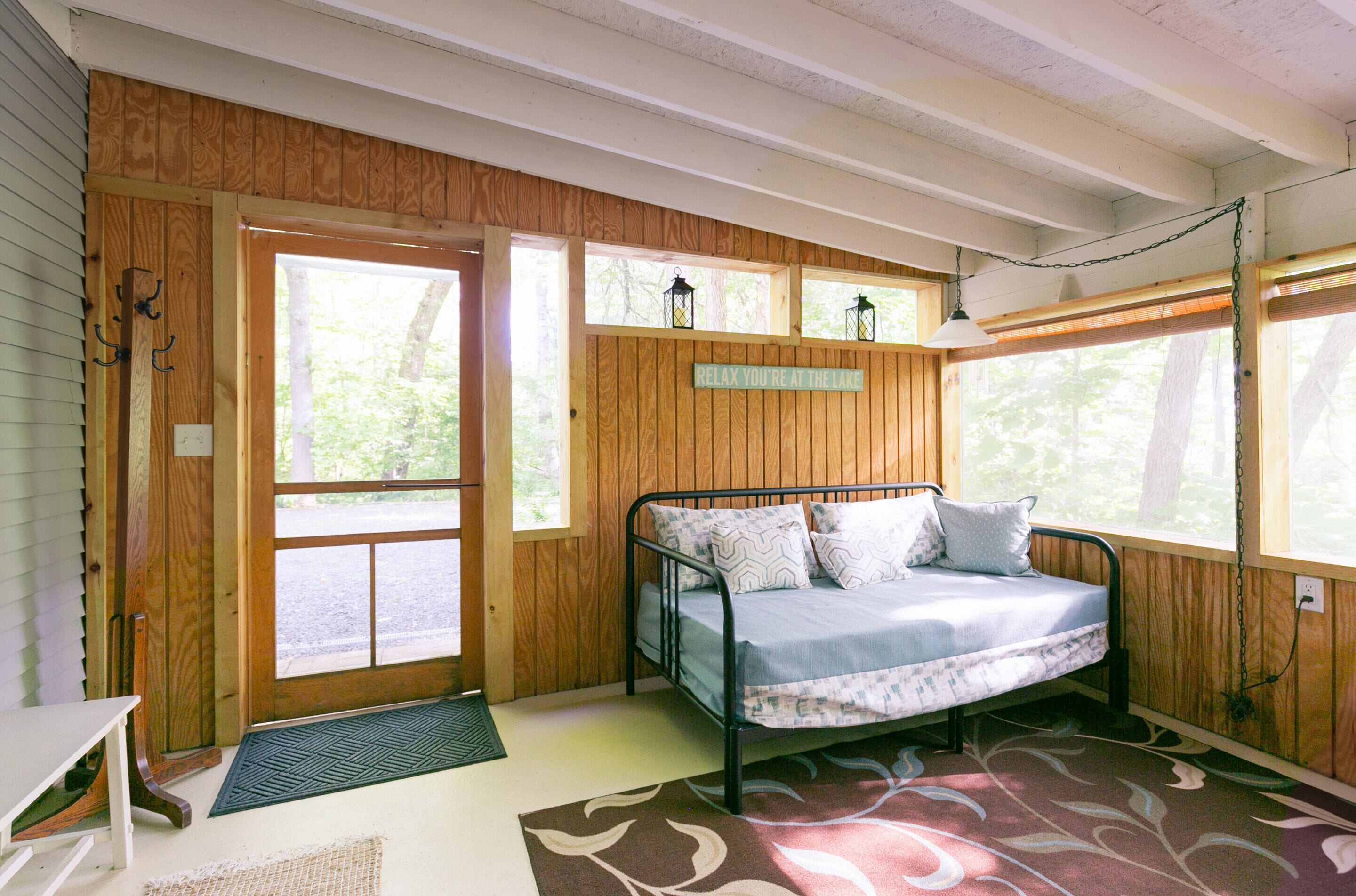 A cozy cabin bedroom with a bed, wooden walls, and large windows.