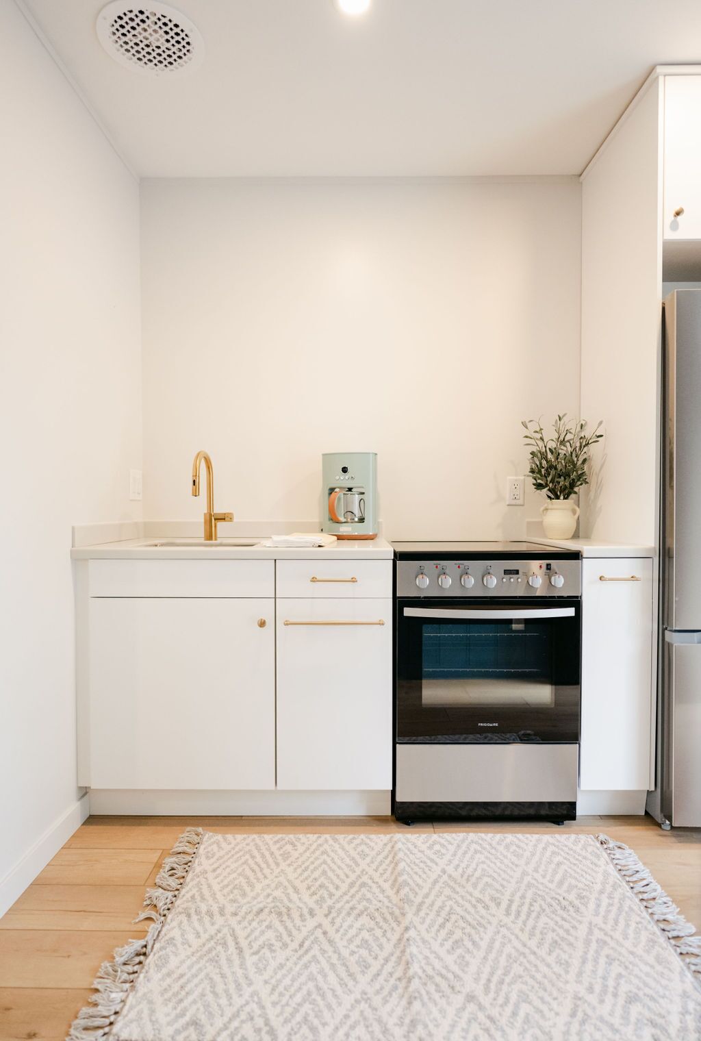 A modern kitchen with white cabinetry, a stainless steel refrigerator, a built-in oven, and a coffee machine.