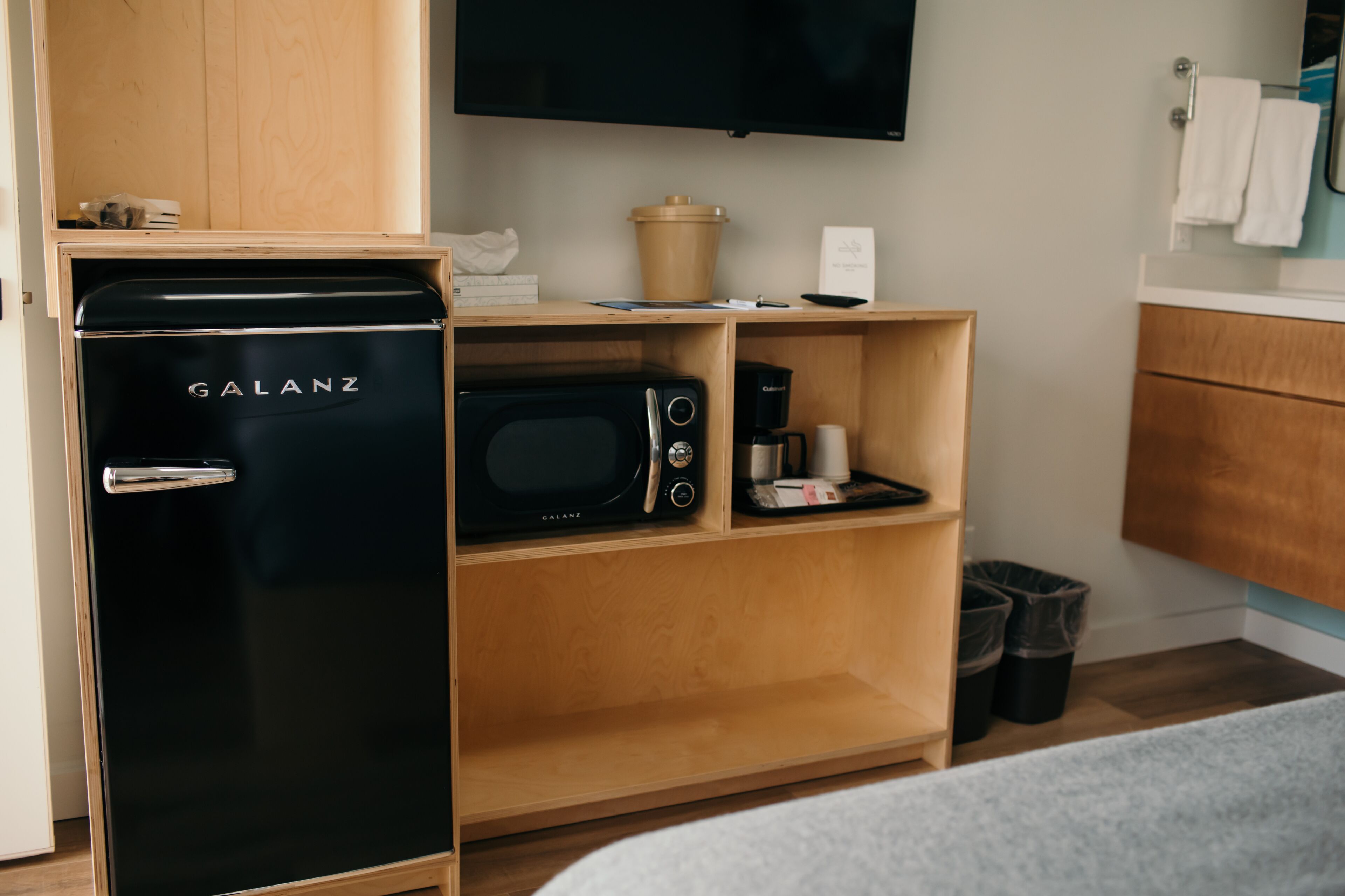 Una kitchenette compacta con un refrigerador Galanz negro, un microondas y una cafetera sobre un estante de madera.