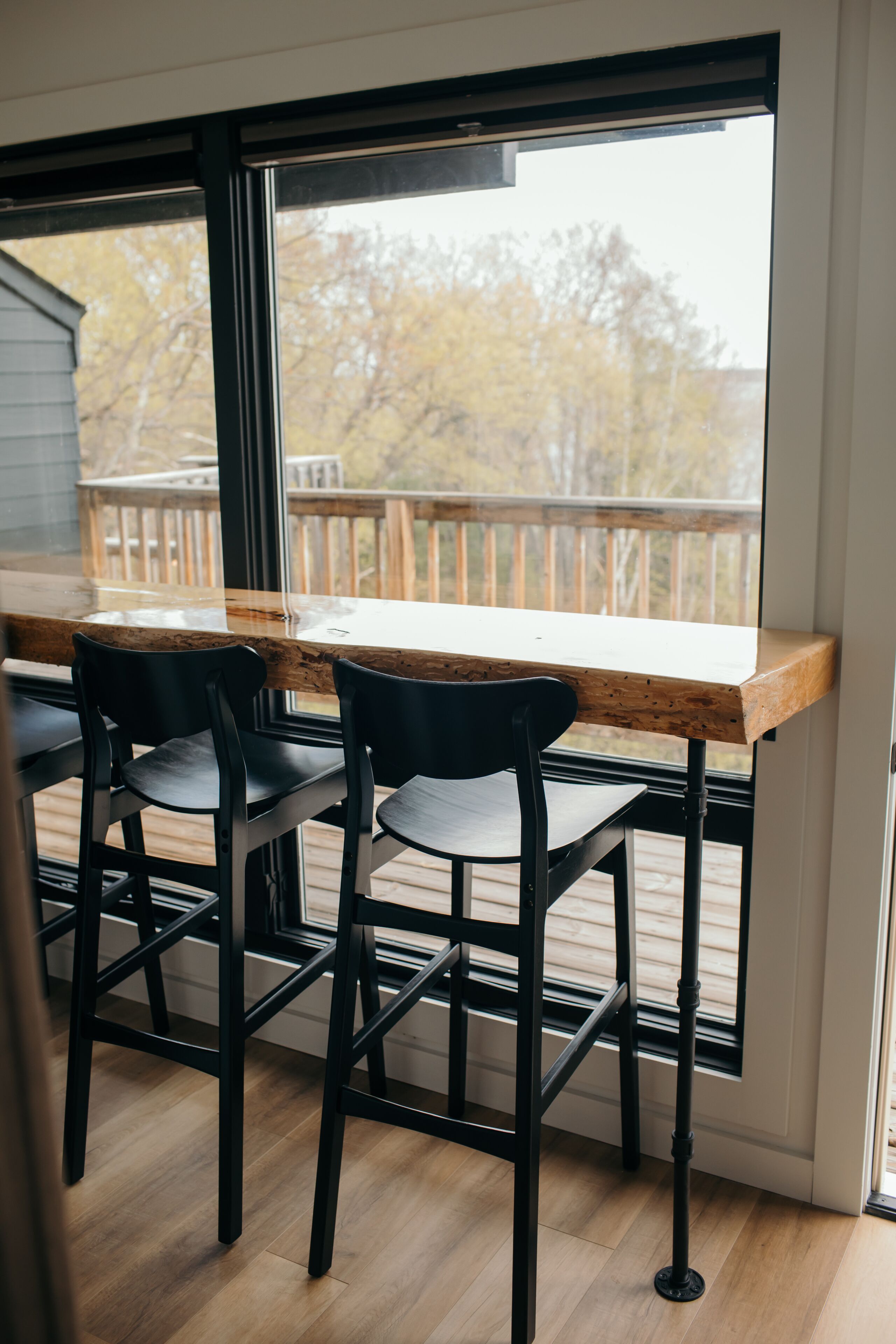 Una terraza de madera con una mesa y sillas, un ventanal grande y vistas a árboles.