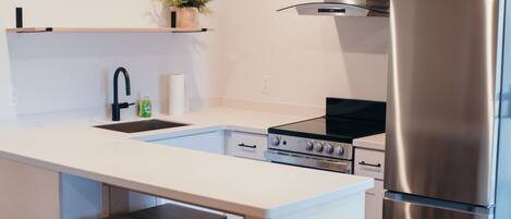 A modern kitchen with a stainless steel refrigerator, a built-in oven, and a sink. There are two wooden stools and a small refrigerator.