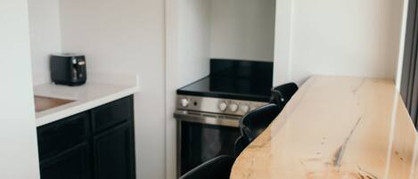 A kitchen with a wooden table, black chairs, a stove, and a coffee maker.