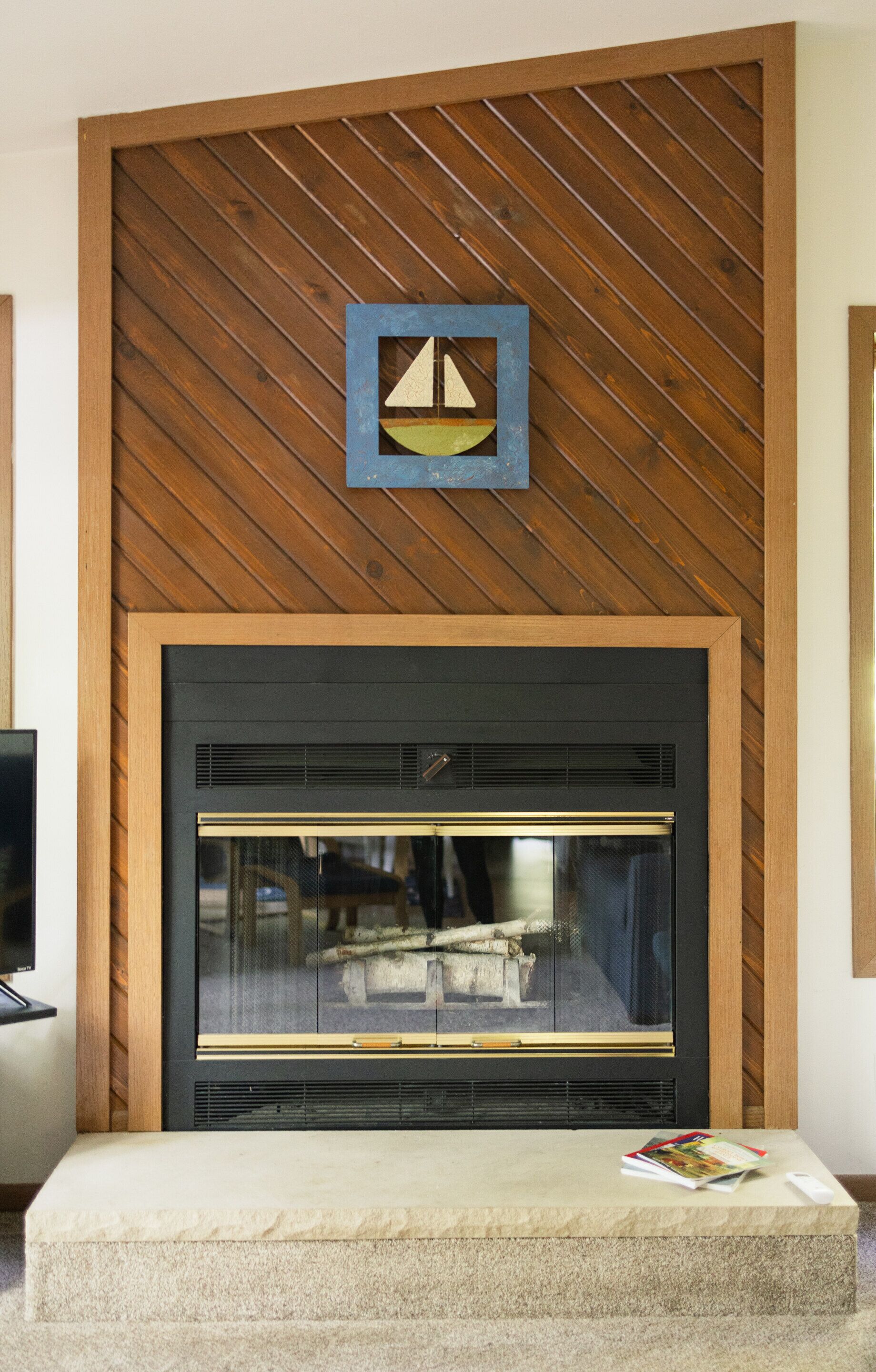A fireplace with a wooden panel wall above it and a magazine on a stone bench in front.