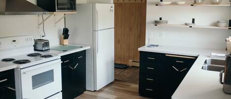 A modern kitchen with white appliances, black cabinets, and wooden flooring.