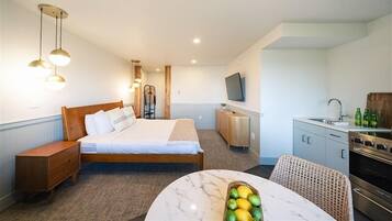 A hotel room with a bed, bedside table, a small kitchenette, a dining area with a table and chairs, and a TV mounted on the wall.