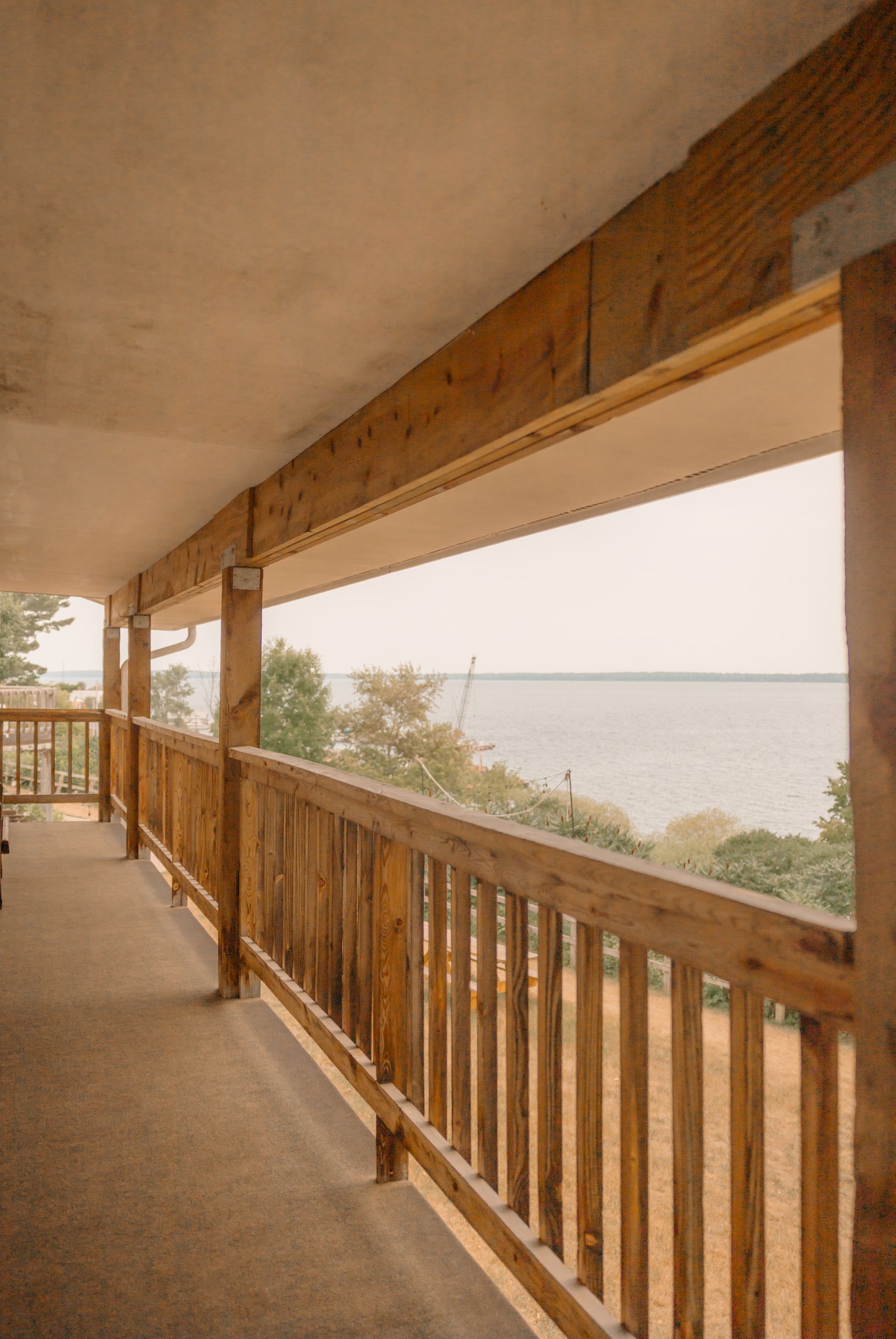 A covered outdoor area with a wooden railing, a concrete floor, and a view of a body of water.