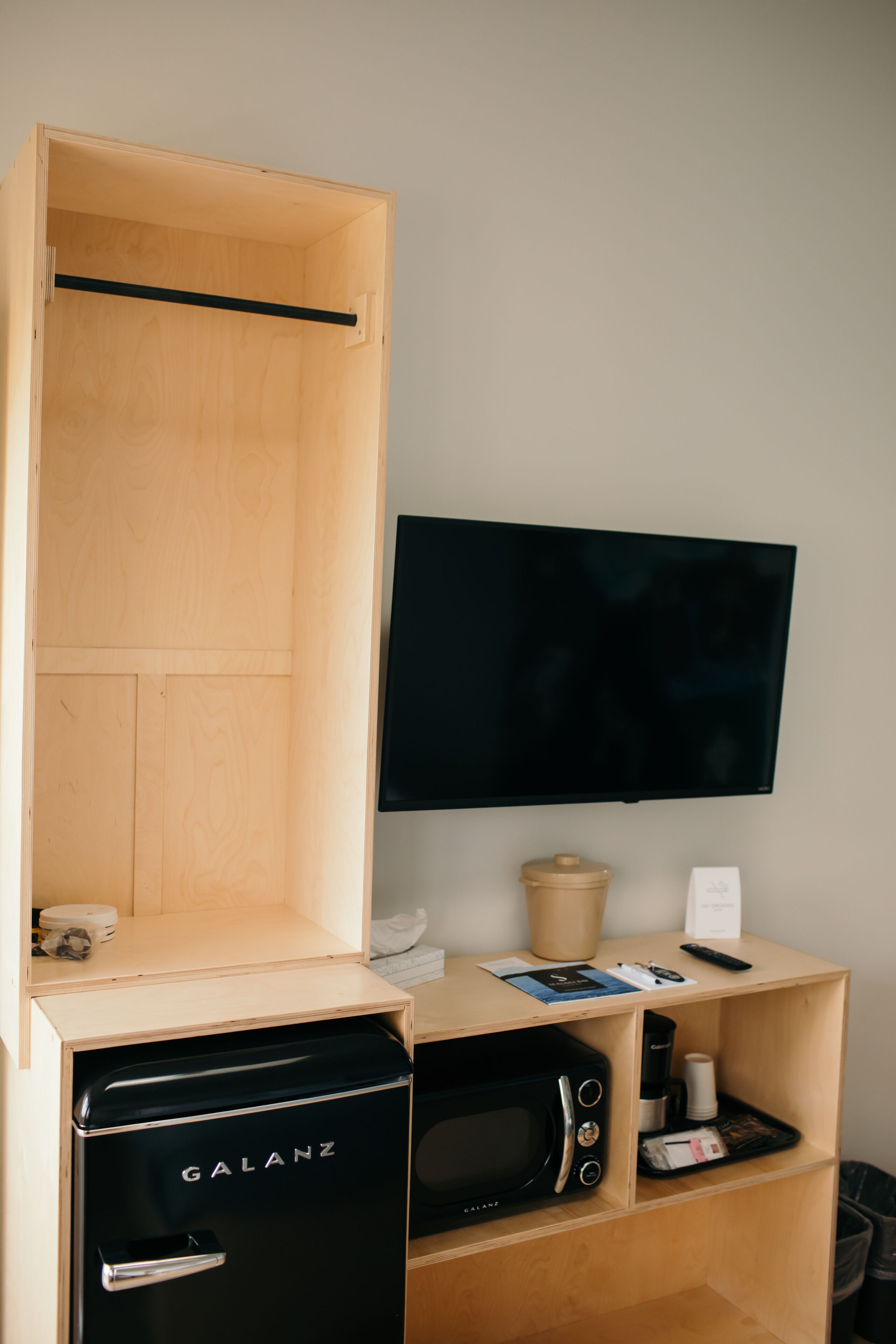 Una habitación funcional con un armario de madera, un televisor de pantalla plana en la pared, un microondas y una cafetera pequeña.