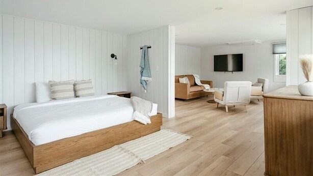 A modern bedroom with a wooden bed, a TV mounted on the wall, and a seating area with a sofa and chairs. - Seagull Bay Motel (Bayfield)
