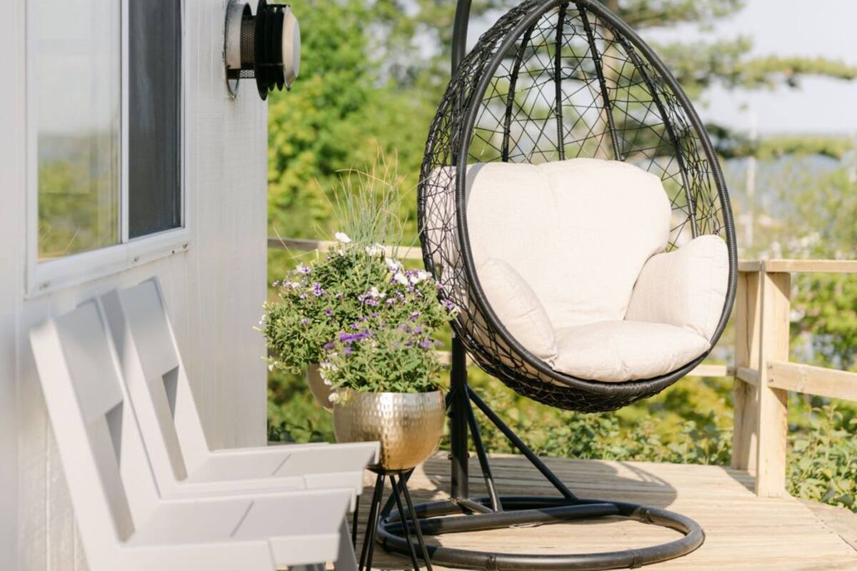 A white house with a hanging chair on a wooden deck, a potted plant, and a window.