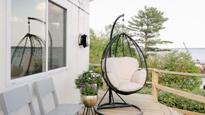 A wooden deck with a hanging chair, two white chairs, and a potted plant. - Seagull Bay Motel (Bayfield)