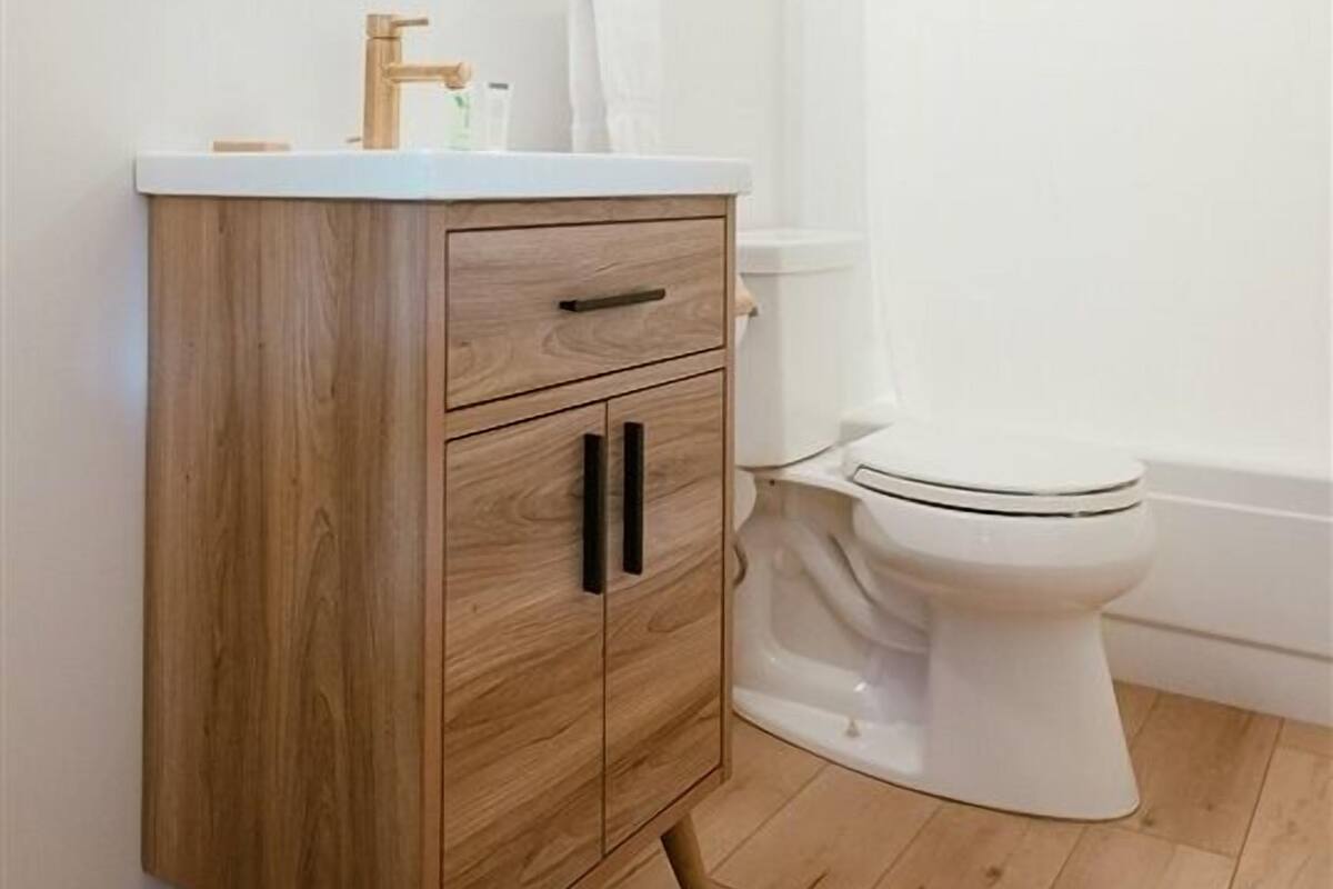 A bathroom with a wooden vanity, a round mirror, a white toilet, and a shower curtain rod.