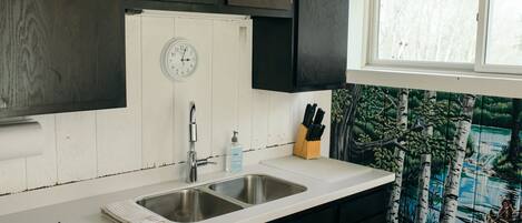 A kitchen with a double sink, dark cabinets, a clock, a window, and a knife block.