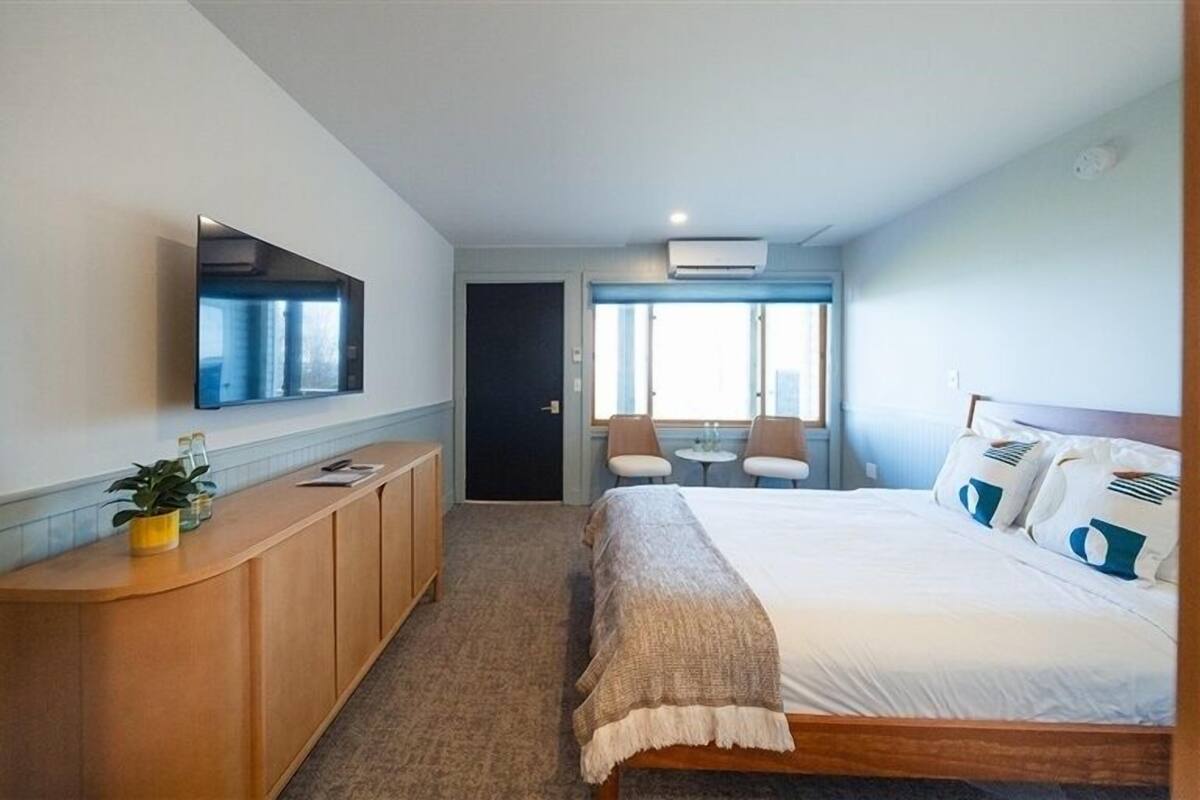 A hotel room with a bed, a desk, a chair, a TV mounted on the wall, and a window with a city view.
