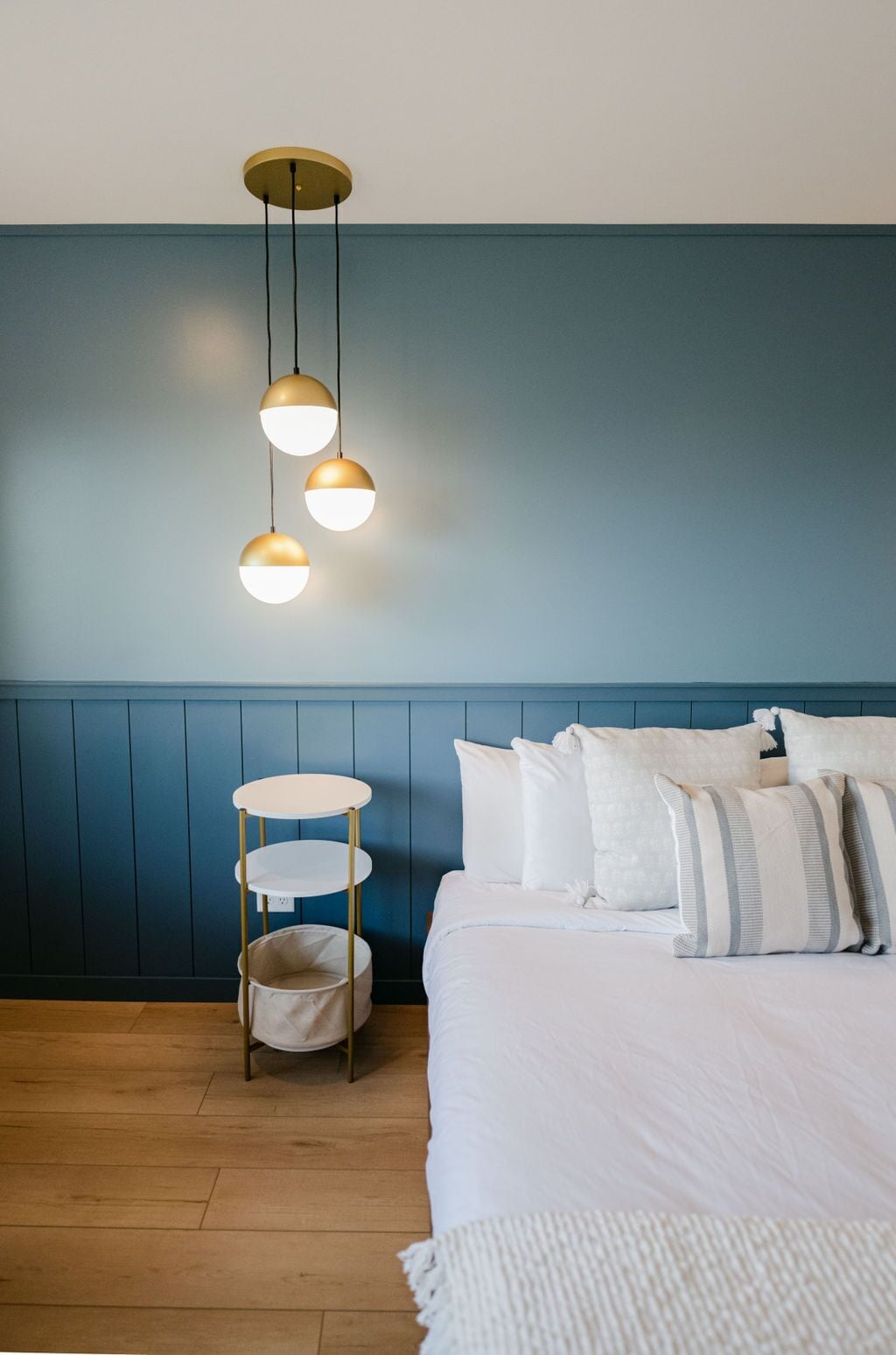 A bedroom with a bed, white bedding, a bedside table with a white lamp, and a blue wall.