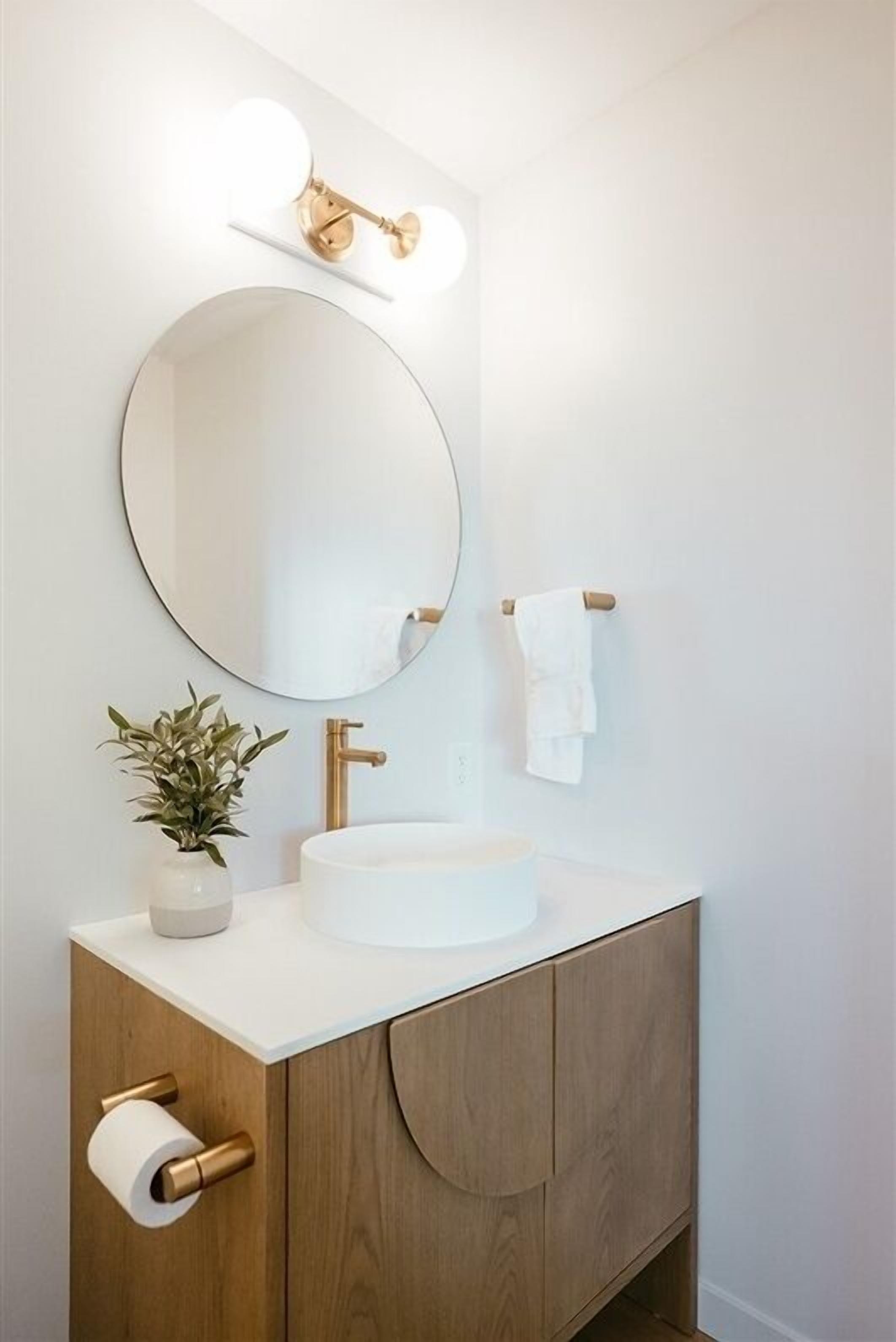 A modern bathroom with a round mirror, a white sink, a wooden vanity, and a towel rack.
