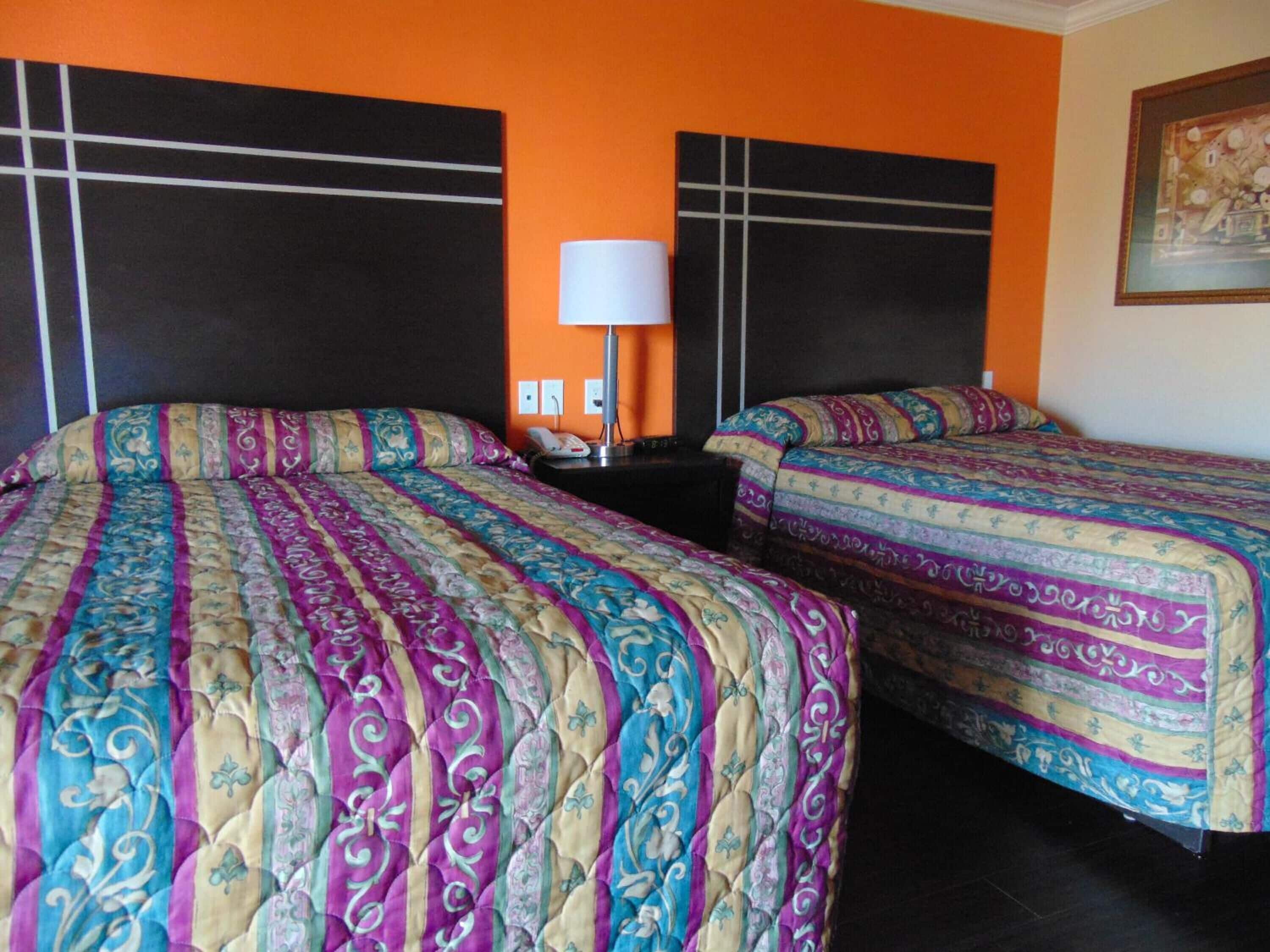 A hotel room with two beds, each with a patterned bedspread, a nightstand with a lamp, and a painting on the wall.