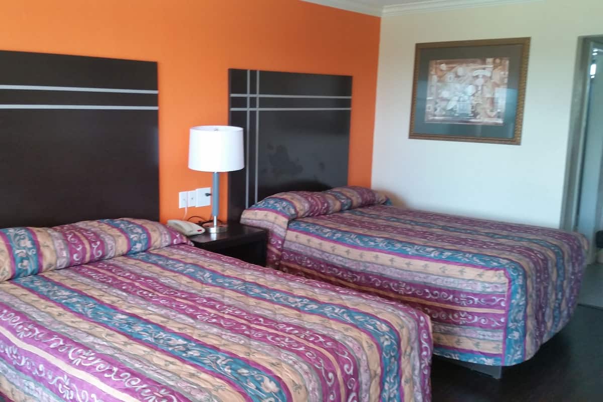 A hotel room with two beds, each with patterned bedding, a bedside table with a lamp, and a framed picture on the wall.