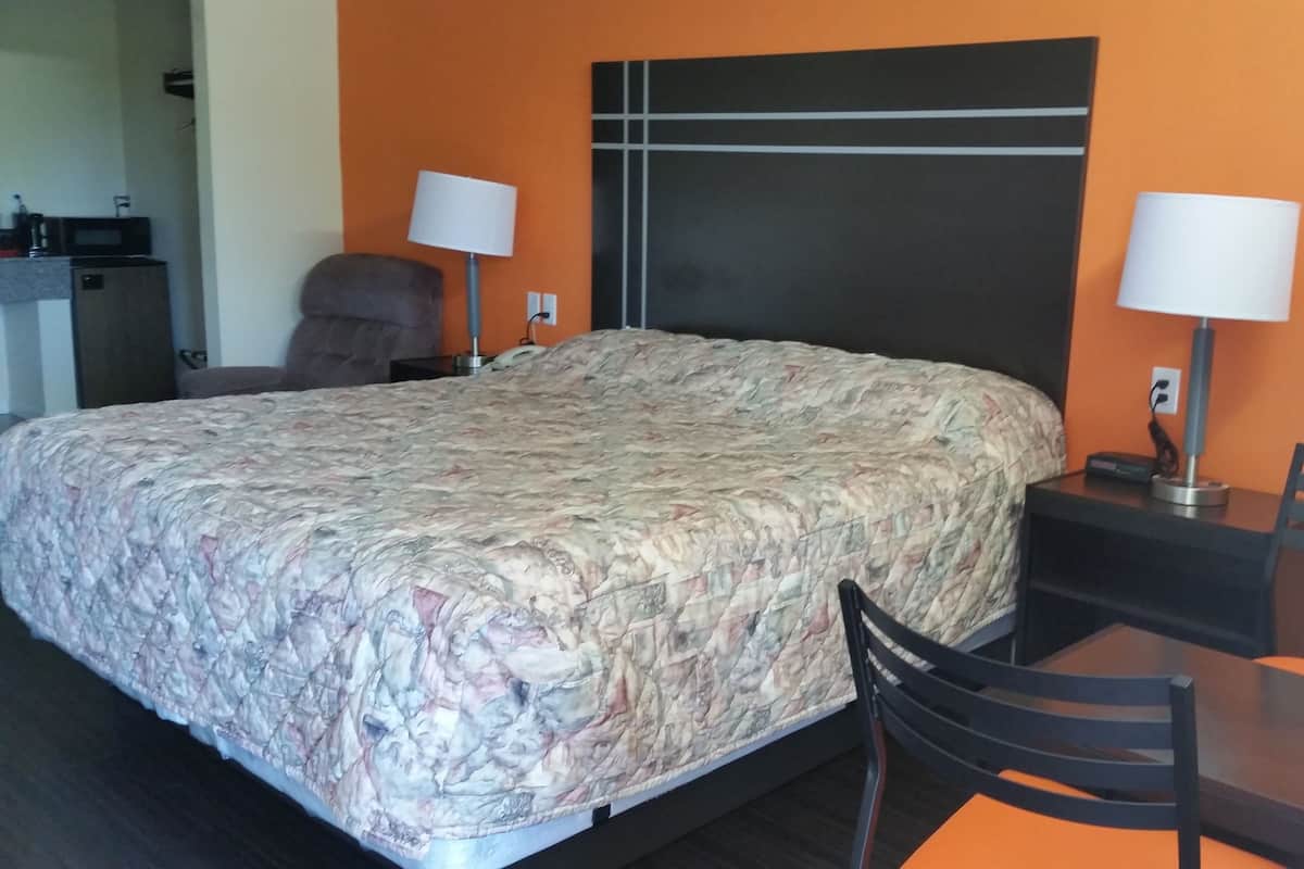 A hotel room with a large bed, a desk with a chair, a lamp, and a microwave in the corner.