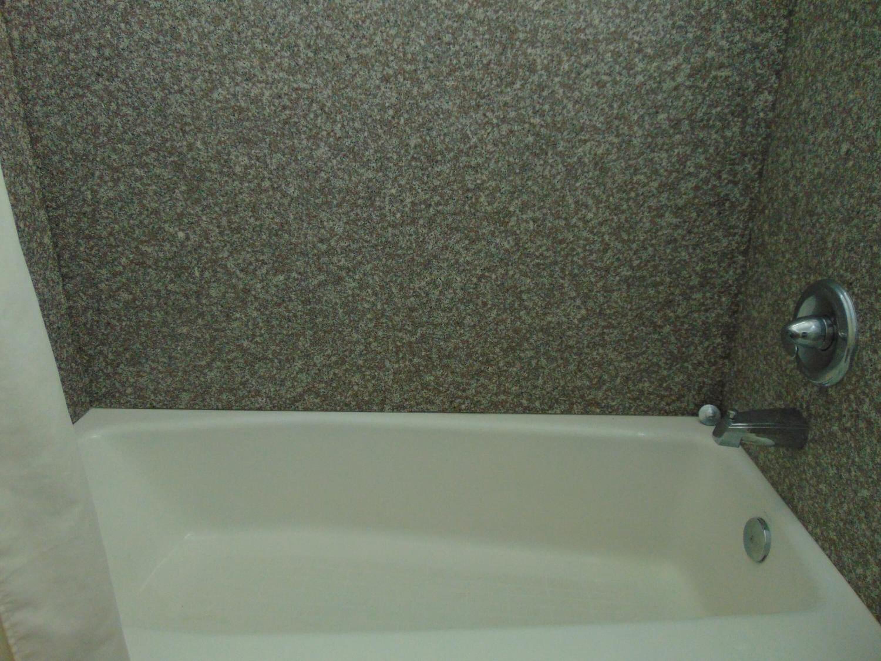 Eine Badewanne mit chromfarbenem Wasserhahn in einem Badezimmer mit gemusterten Steinwänden.