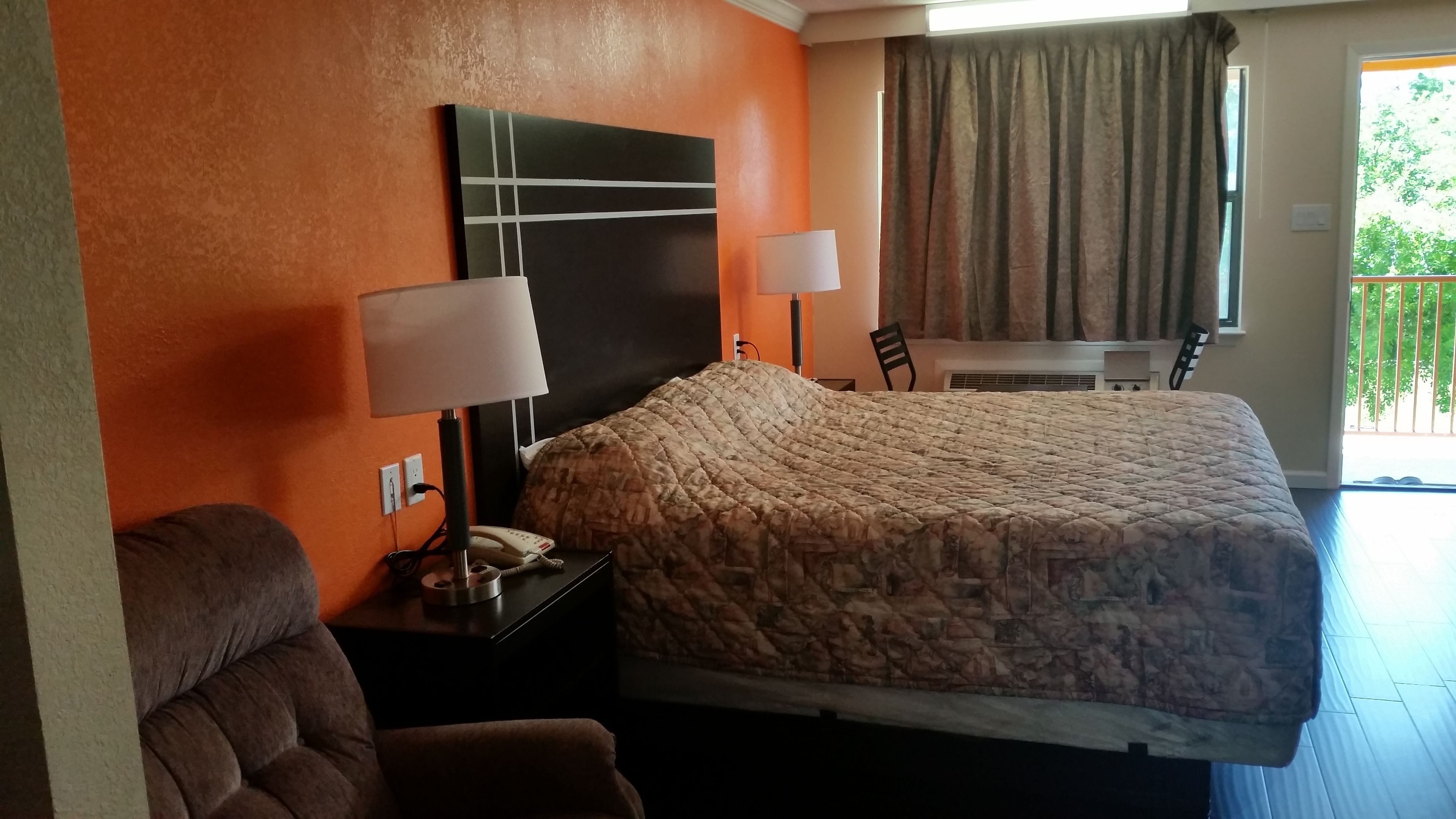 A hotel room with a bed, a chair, a desk, and a window with curtains.