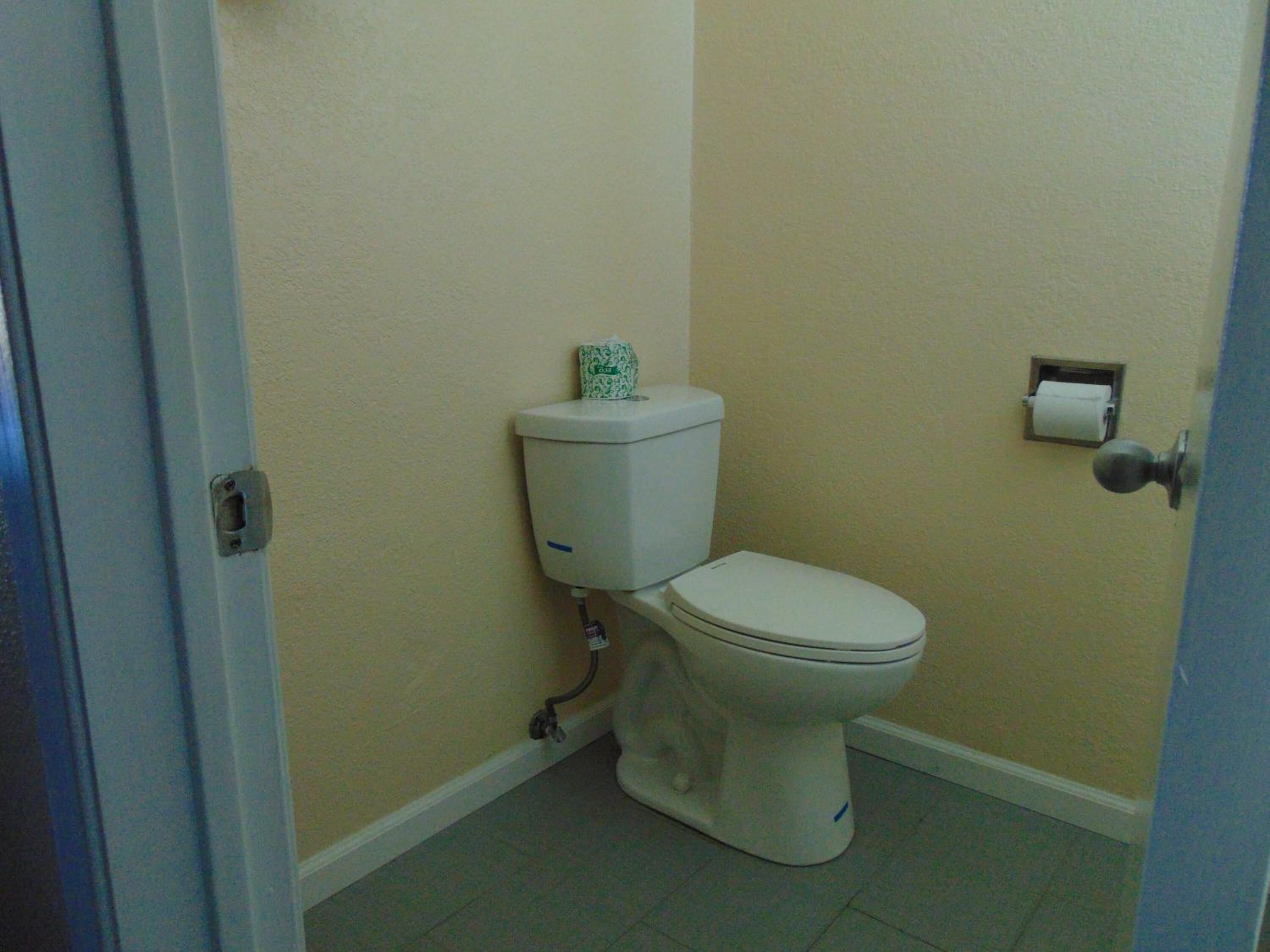 A small, simple bathroom with a toilet, a paper towel dispenser, and a plain wall.